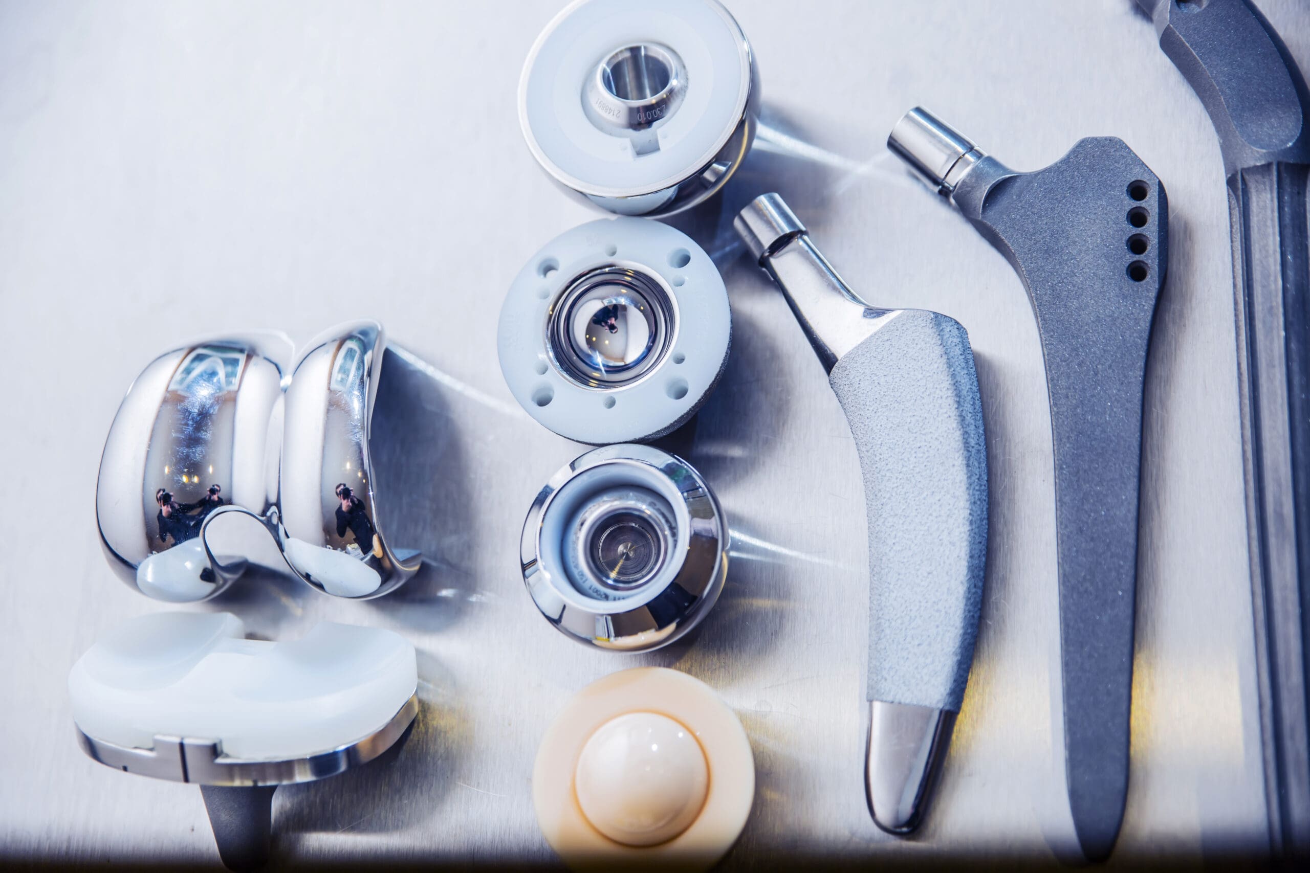 A set of various orthopedic implants made of metal and ceramic, including components of artificial hip and knee joints, displayed on a stainless steel surface.